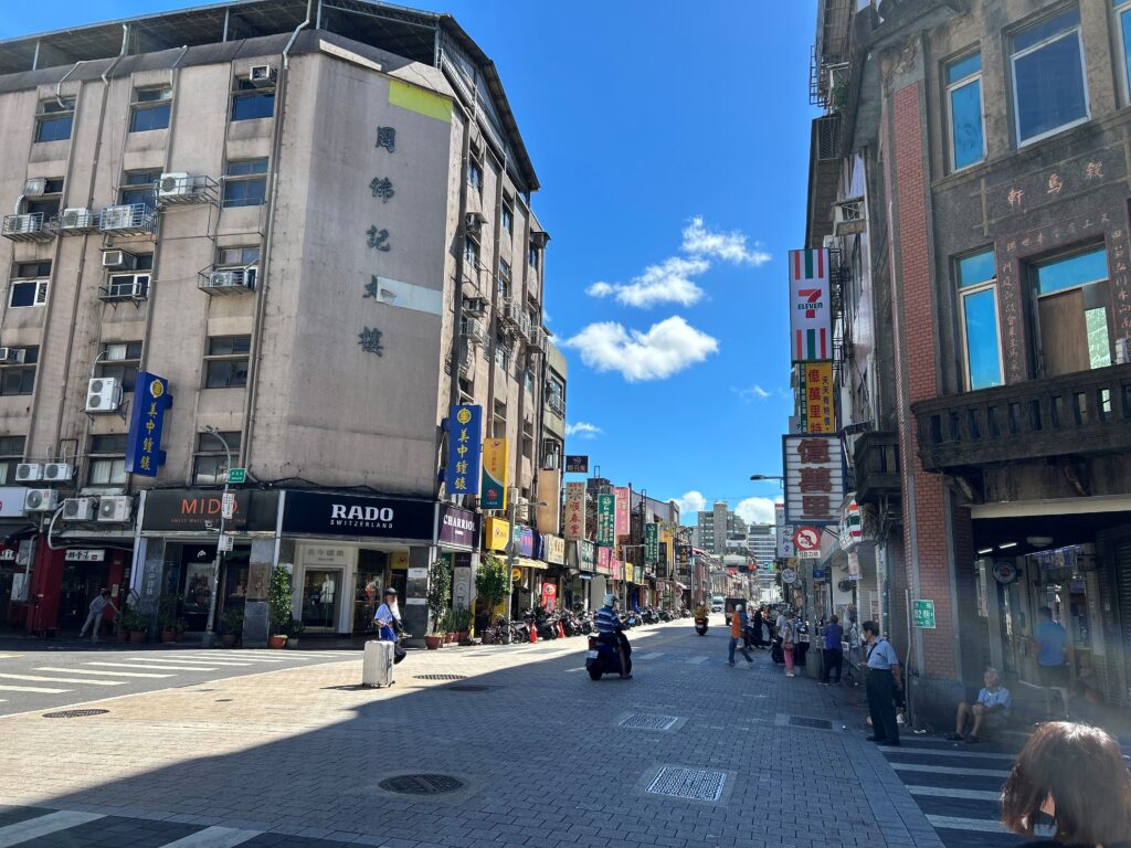 台湾の街並み。両脇には歴史を感じる5階建てほどのビル。道路はレンガでできており、右手にはセブンイレブンも見える