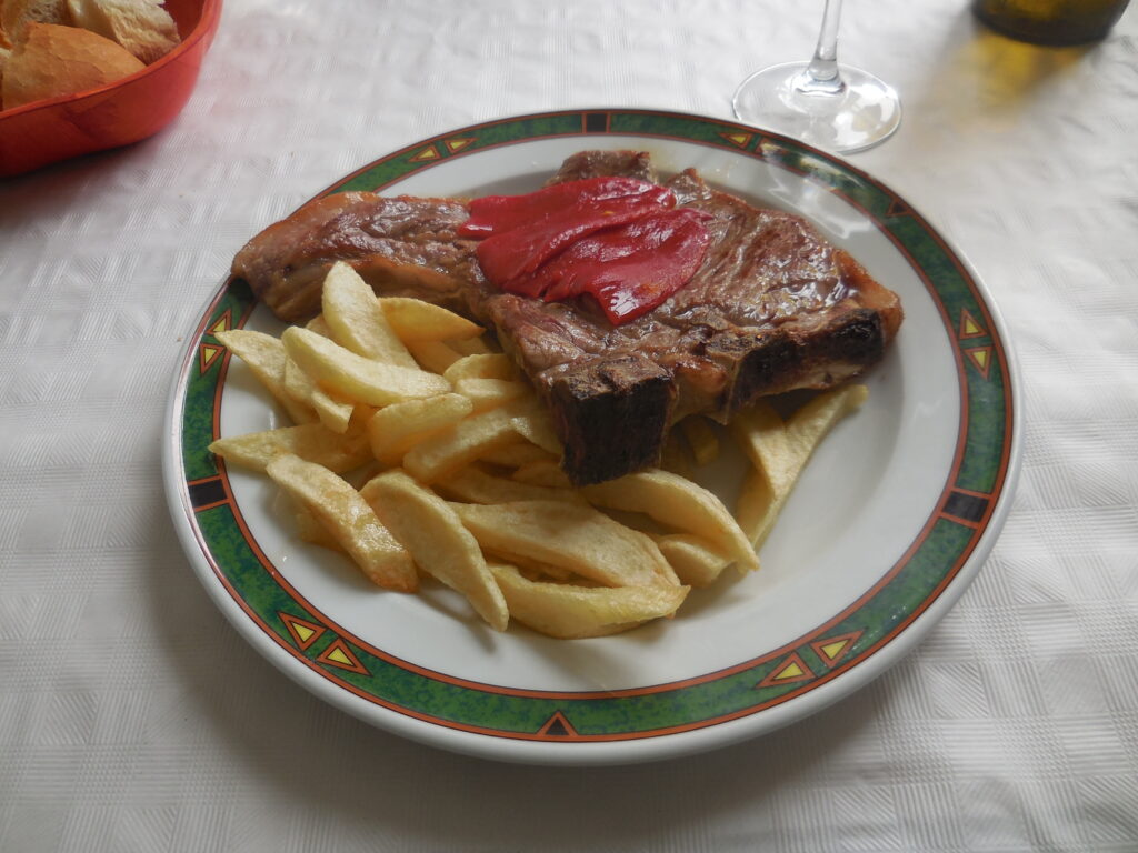 料理写真。炭火で焼いた牛肉の上に赤パプリカ。脇にフライドポテトが添えられている