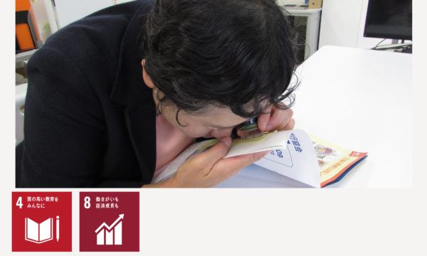 画像：ルーペで冊子を読む視覚障害者の女性